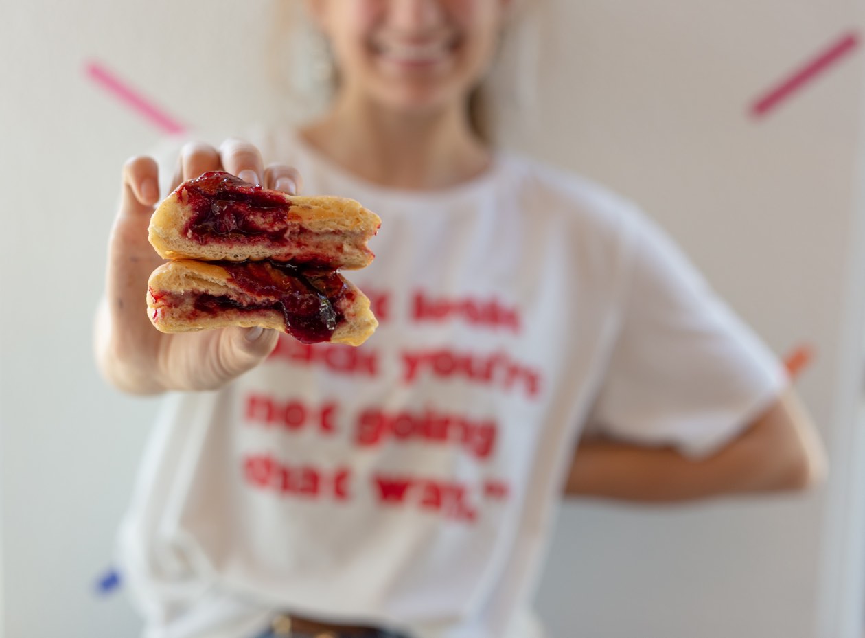 A picture of a person holding a baked good with jam into the camera.