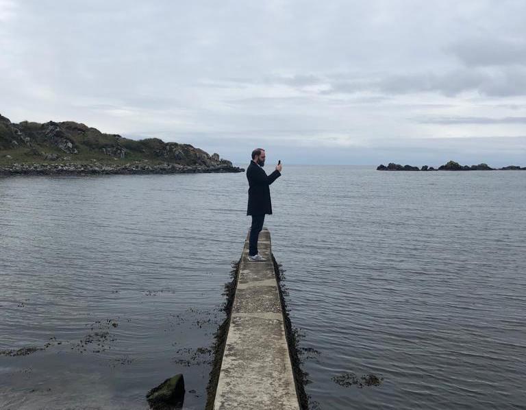 Picture of Florian holding his phone with the ocean in the background.